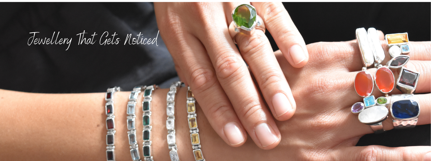 Woman wearing bold sterling silver jewellery including chunky silver bangles, a large natural gemstone ring and a statement pendant from Desiderate Jewellery.